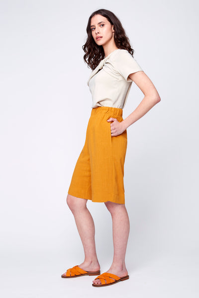 Bermuda Ivy de JULEI, en lin soyeux éco-responsable. Élastique à la taille, poches sur le coté, gousset a l'entrejambe. Couleur safran. Porté avec le haut Monica